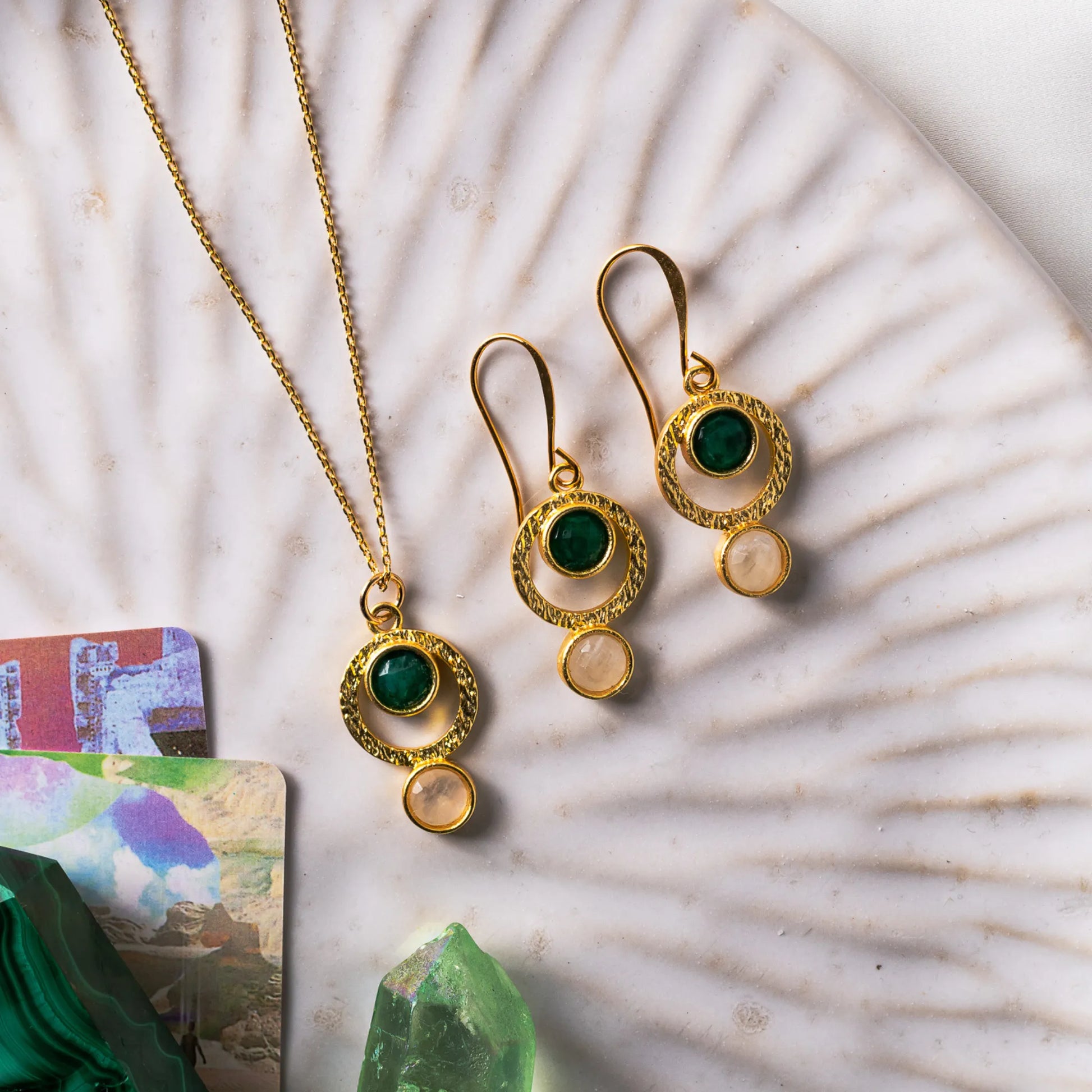 Gold-plated pendant necklace and matching earrings featuring brushed sacred geometry-inspired circle patterns. The pendant and earrings are adorned with vibrant emerald and luminous moonstone stones, symbolizing growth, intuition, and unity.