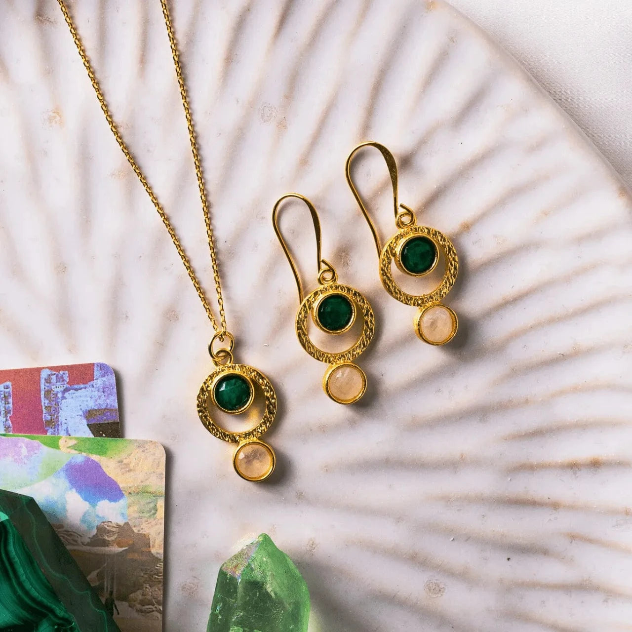 Gold jewelry set with green gemstones on a textured surface
