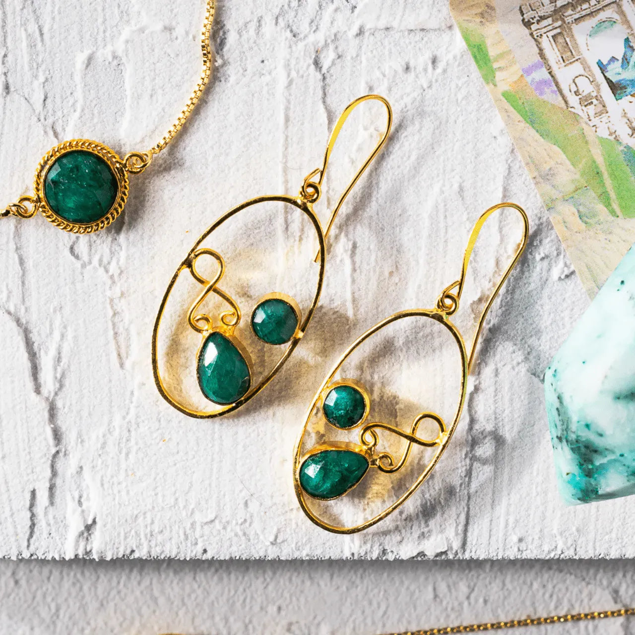 Gold earrings with green gemstones on a textured white surface