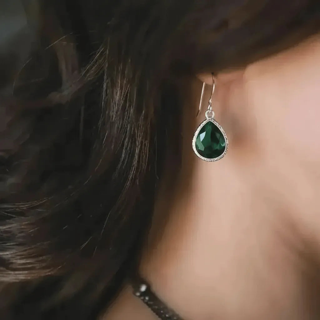 Close-up of a person wearing green teardrop earrings with blurred background