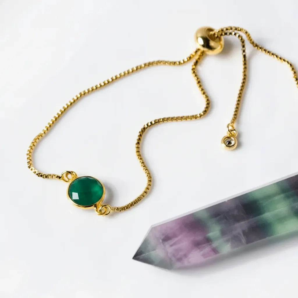 Gold bracelet with a green gemstone next to a crystal on a white background
