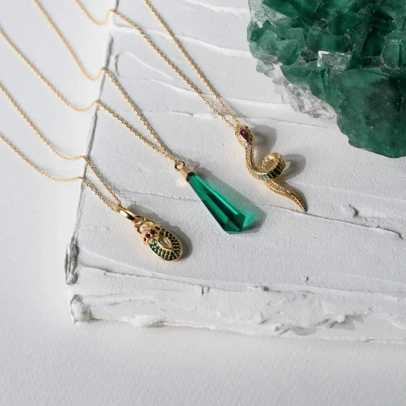 Gold necklaces with various pendants on a white surface with green crystals.