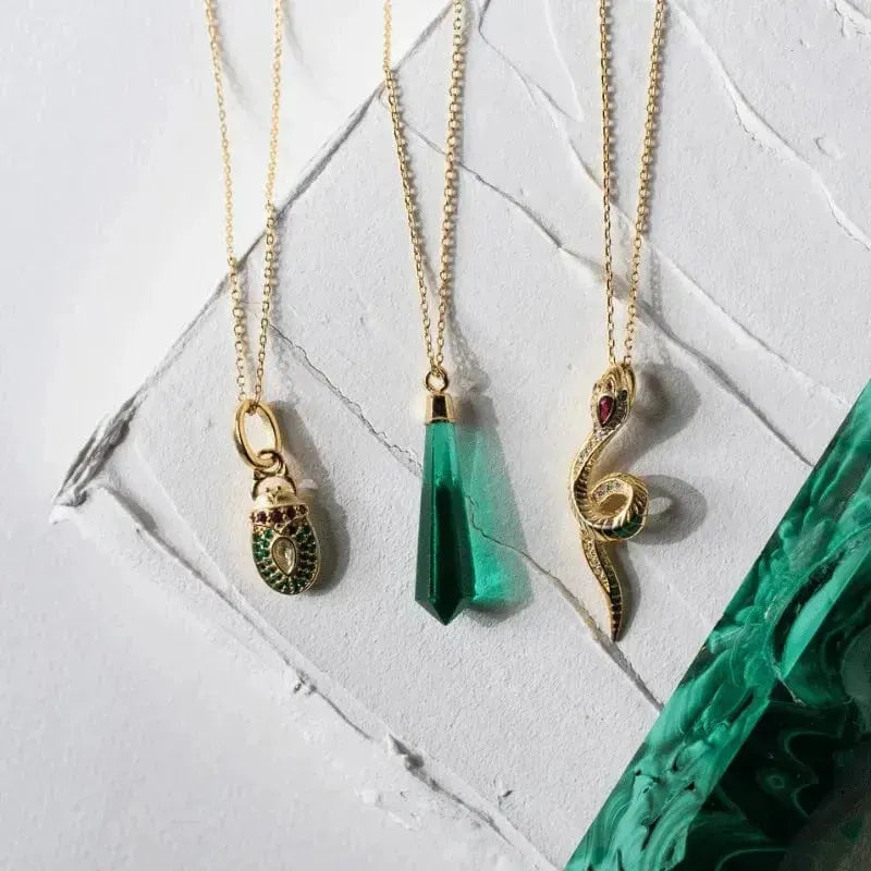 Three gold necklaces with unique pendants on a textured white surface.