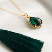Gold necklace with a green gemstone pendant on a white background