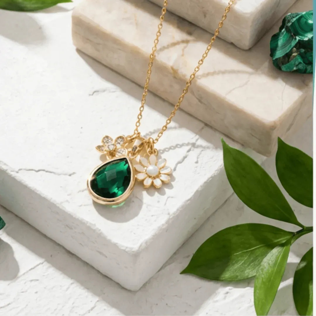 Gold necklace with a green pendant on a white surface with green leaves.