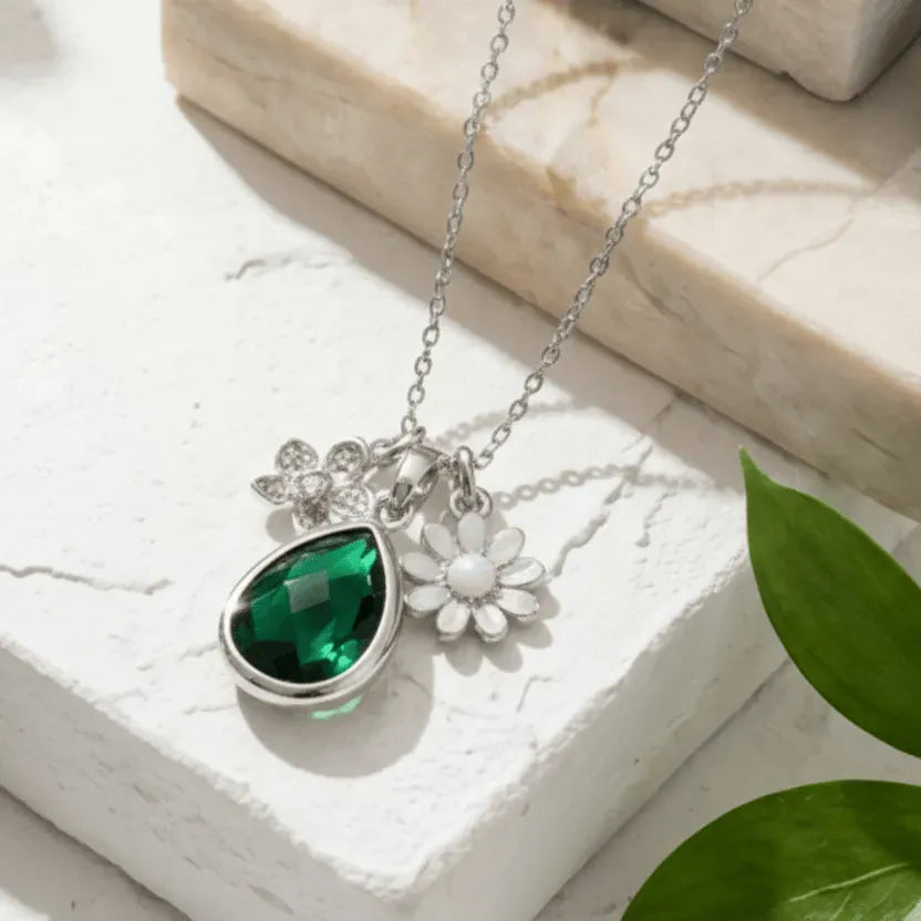 Necklace with green teardrop pendant and white flower charm on a light surface.