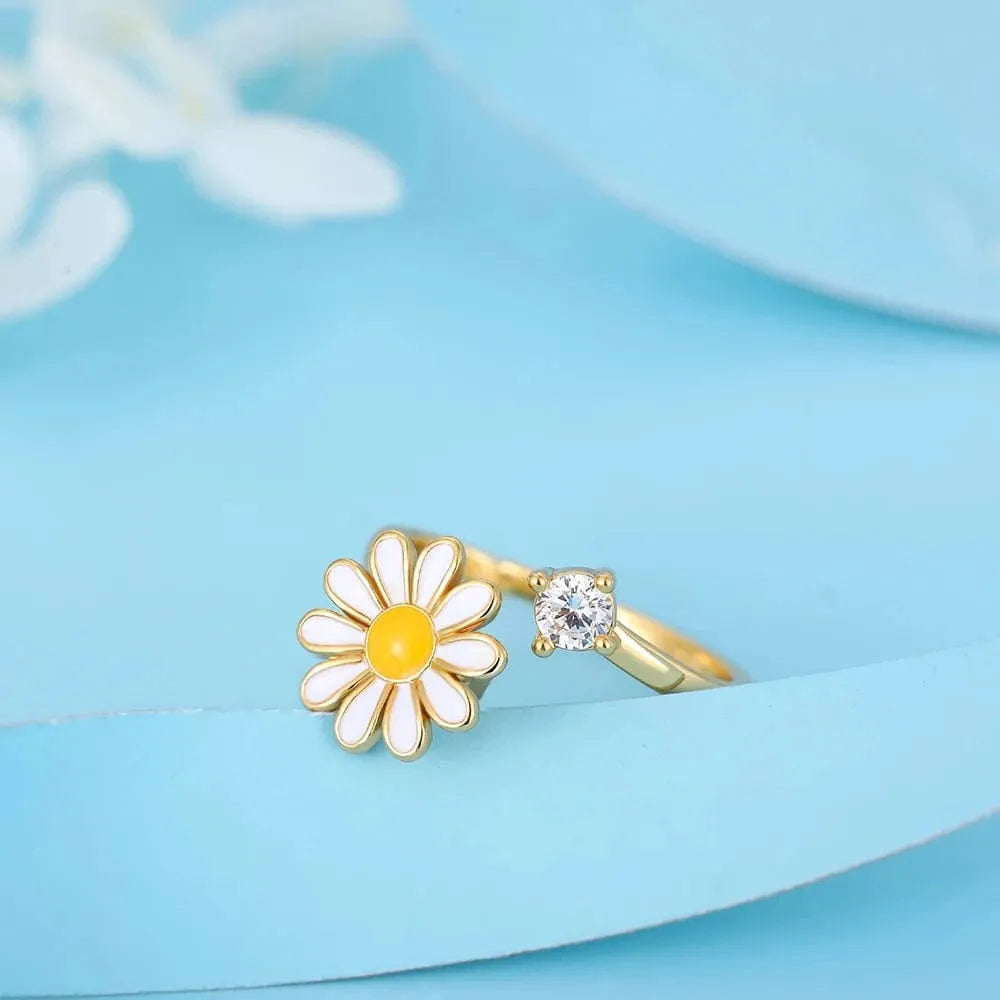 Gold ring with a daisy flower and gemstone on a light blue background