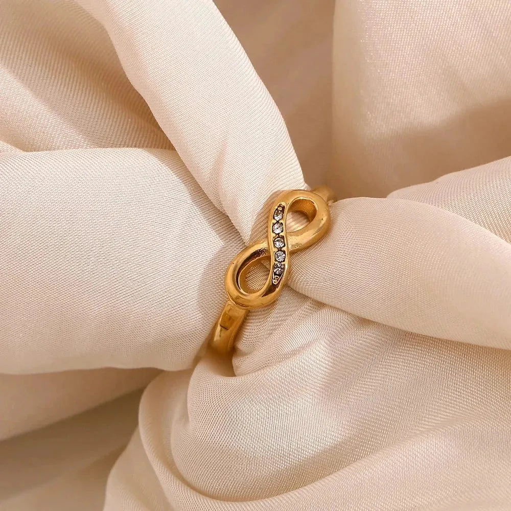 Gold infinity ring with embedded stones on a beige fabric background