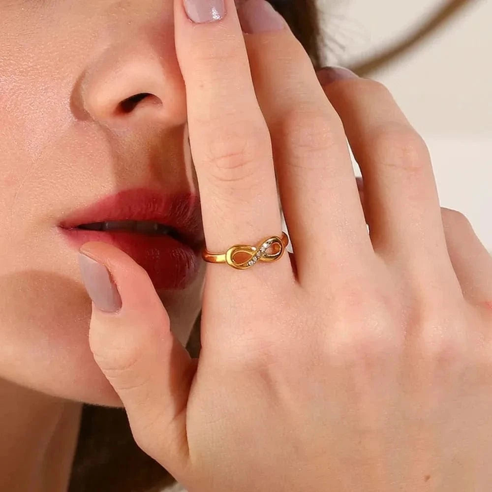 Close-up of a hand wearing a gold ring with a red stone, touching the face.