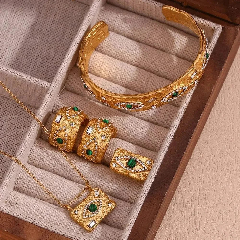 Gold jewelry set with green gemstones on a textured surface