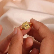 Gold ring with a sunflower design held between fingers against a soft beige background