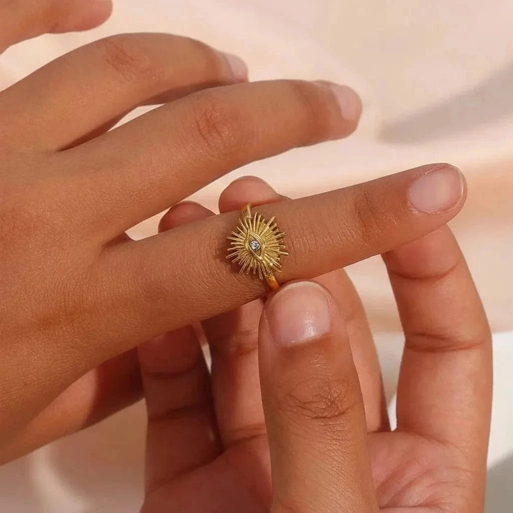 Gold ring with a sunflower design on a person's finger against a soft pink background