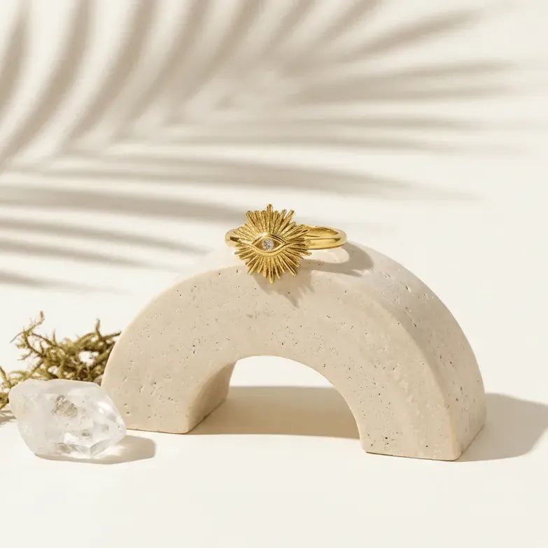 Gold ring with a sun design on a beige arch-shaped stand against a light background