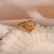 Gold ring with eye design on a textured beige surface