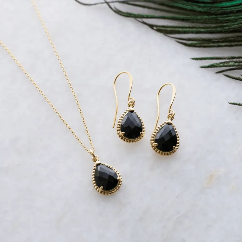 Gold necklace and earrings with black stones on a marble surface