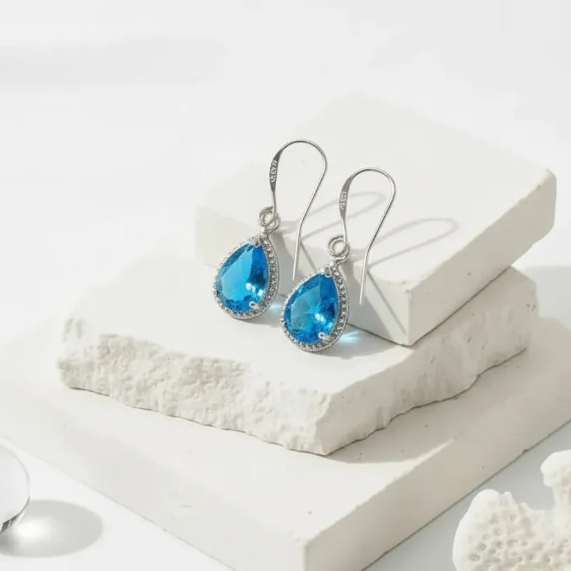 Blue teardrop earrings on a white surface with coral-like texture
