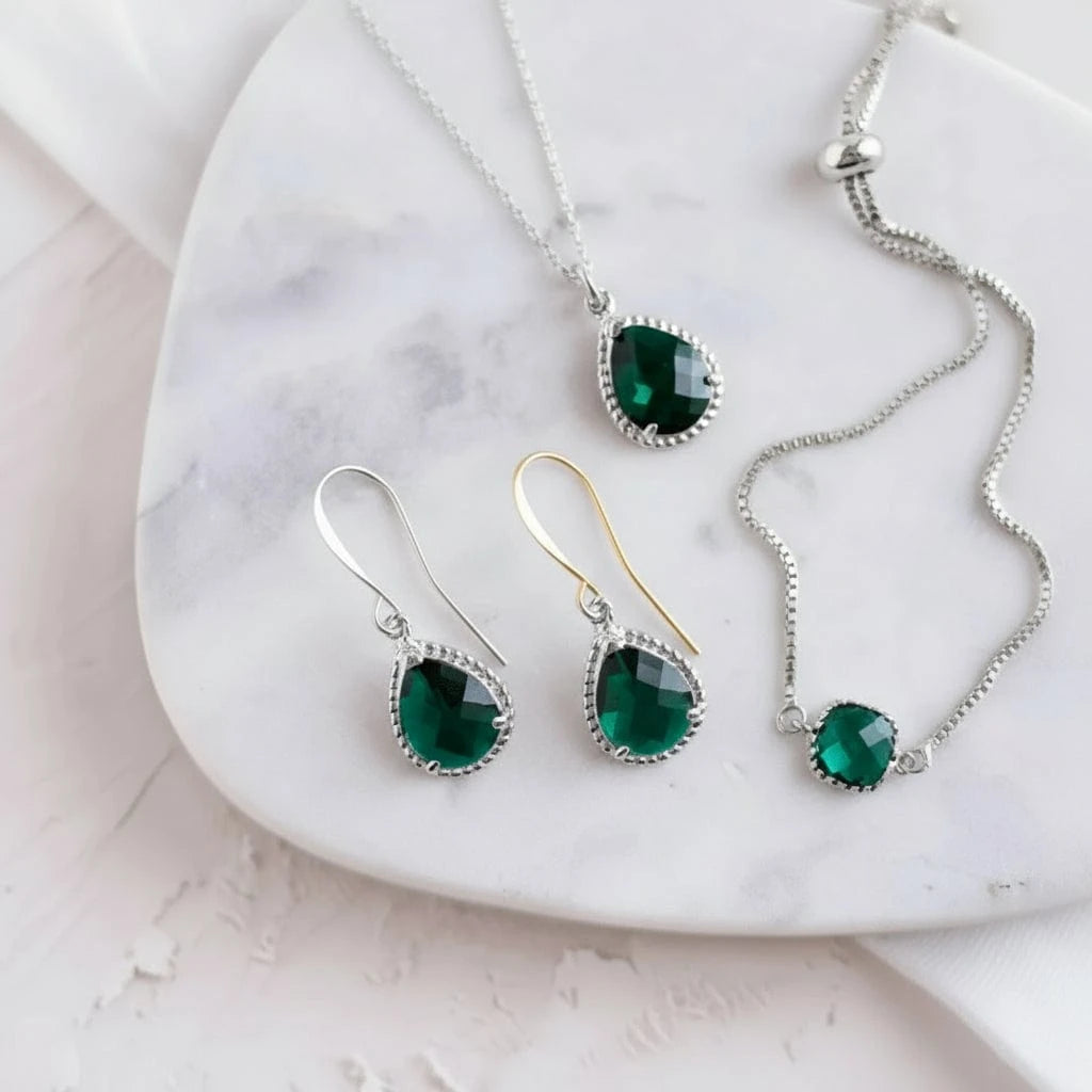 Gold jewelry set with green gemstones on a marble surface