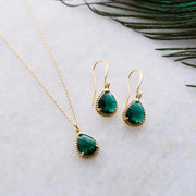 Gold necklace and earrings with green gemstones on a marble surface.