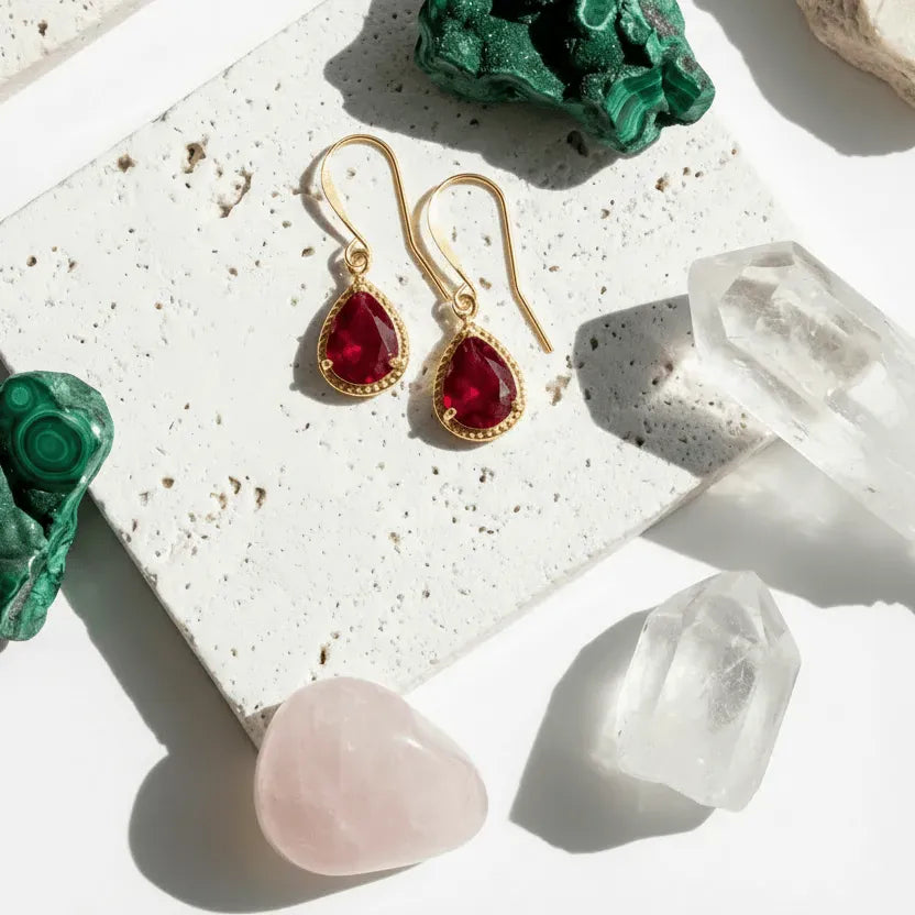 Gold earrings with red gemstones on a surface with crystals and stones.