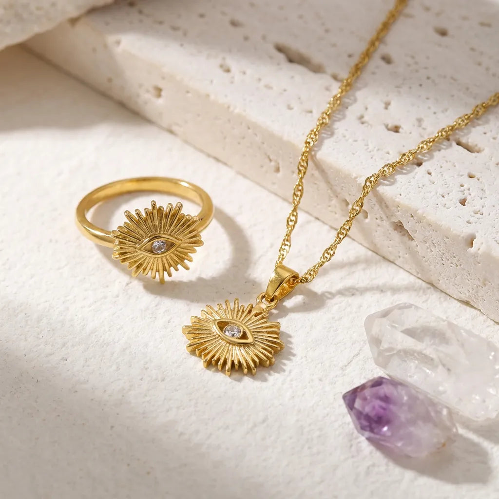 Gold ring and necklace with an eye design on a textured surface with crystals.