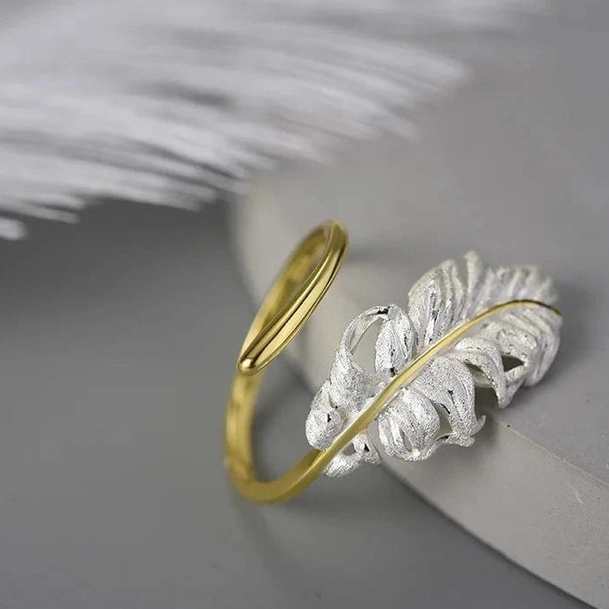 Gold and silver leaf-shaped rings on a gray surface with white feathers.