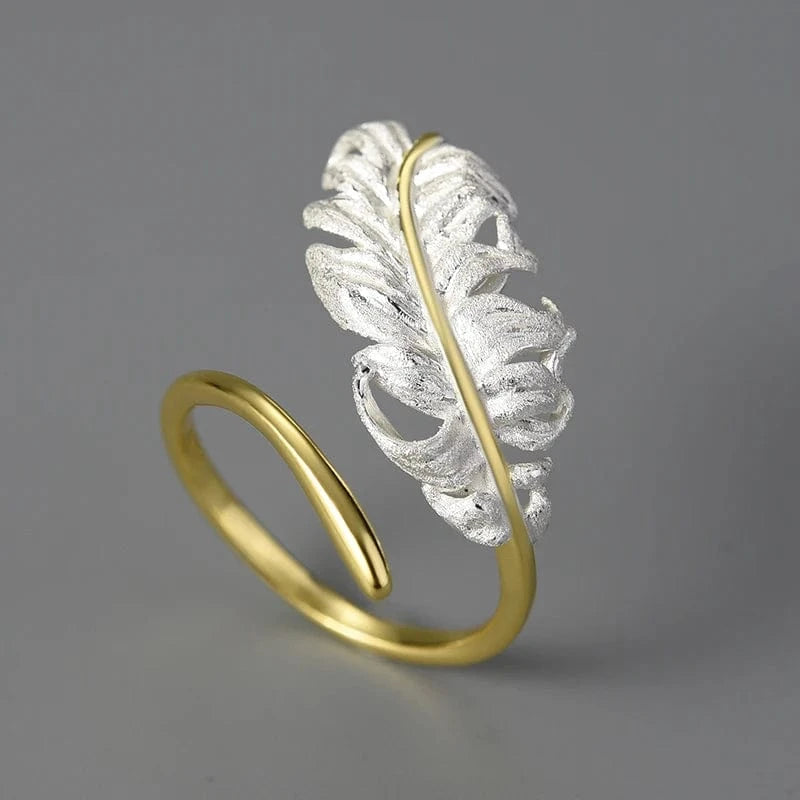 Gold and silver feather-shaped ring on a gray background