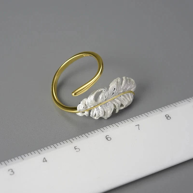 Gold and silver feather-shaped bracelet on a gray background with a ruler for scale.