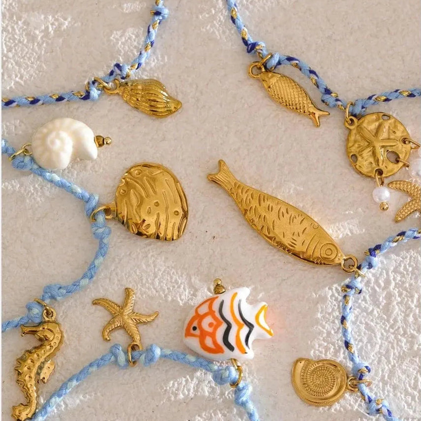 Decorative string with gold fish, starfish, and seahorse charms on a textured beige background.