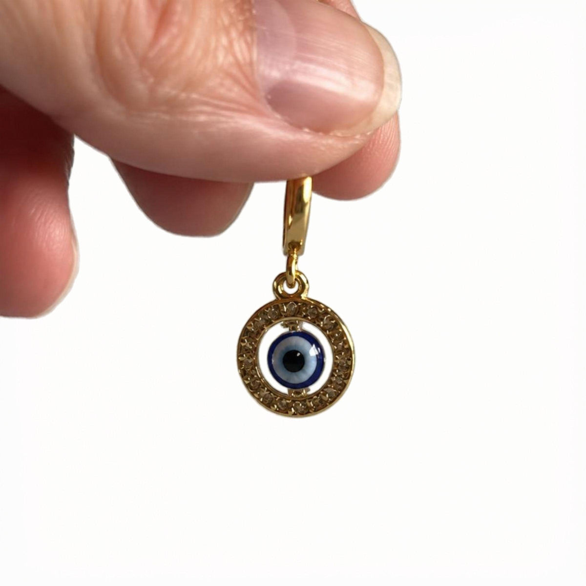 Fingers holding the gold floating evil eye pendant, shown for scale