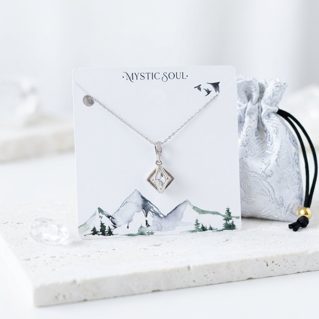 Silver Floating Prism necklace, an open 3D geometric frame with a clear faceted glass bead, on a Mystic Soul jewelry card beside a satin pouch