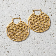 Gold hoop earrings with intricate geometric design on a white stone