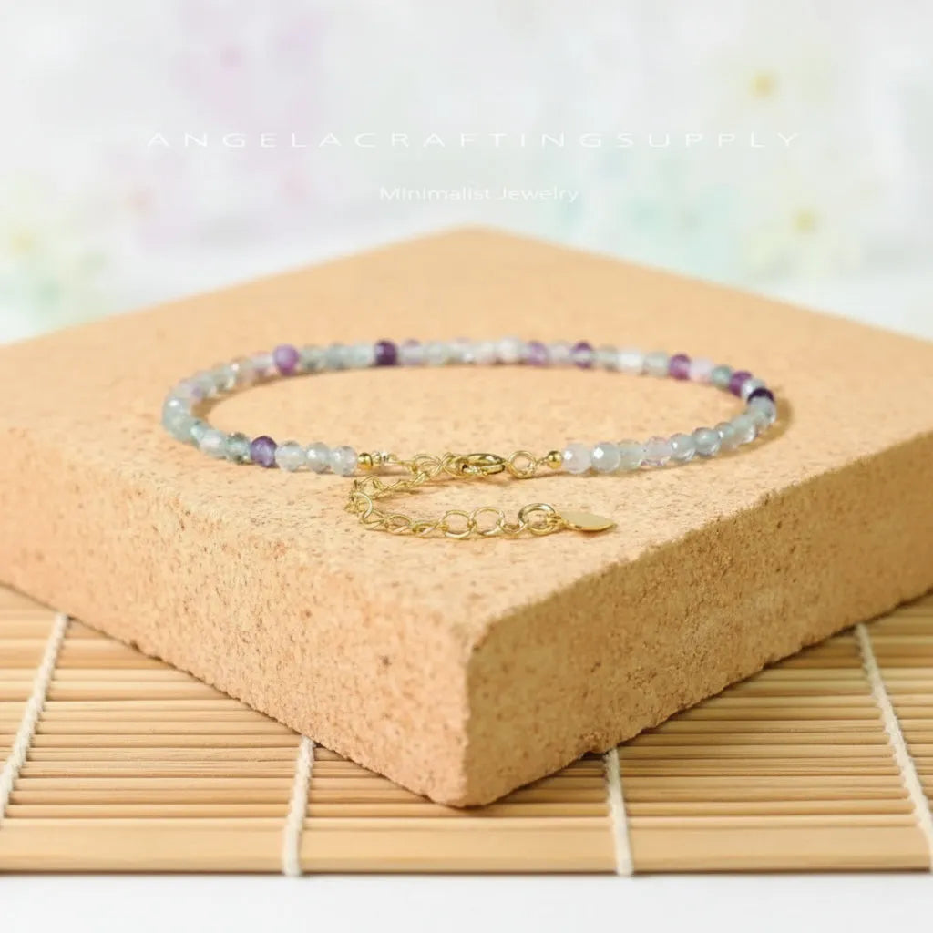 Beaded bracelet with gold chain on a wooden block with flowers in the background