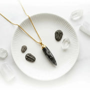 Necklace with a black pendant on a white plate with trilobite fossils and crystals.