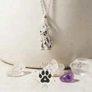 Silver dog-shaped pendant necklace on a chain with crystals and a white bowl in the background.
