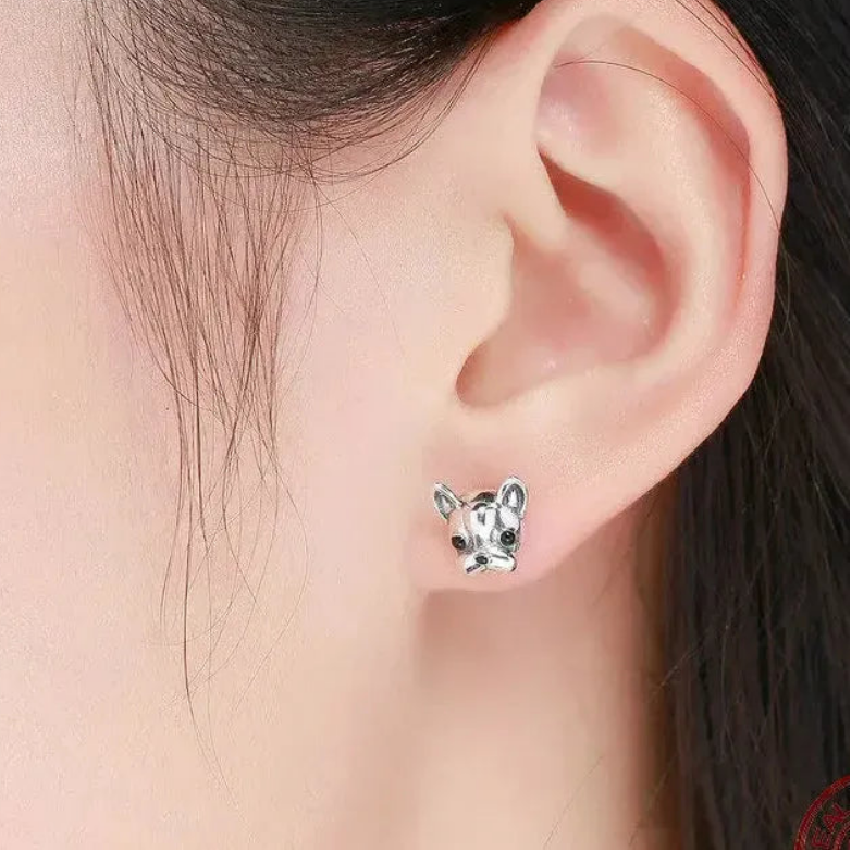 Silver dog-shaped earrings worn by a person with dark hair.