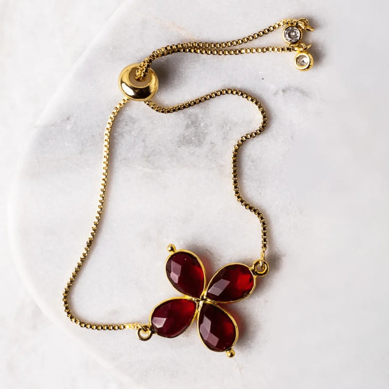 Gold necklace with a red pendant on a marble surface