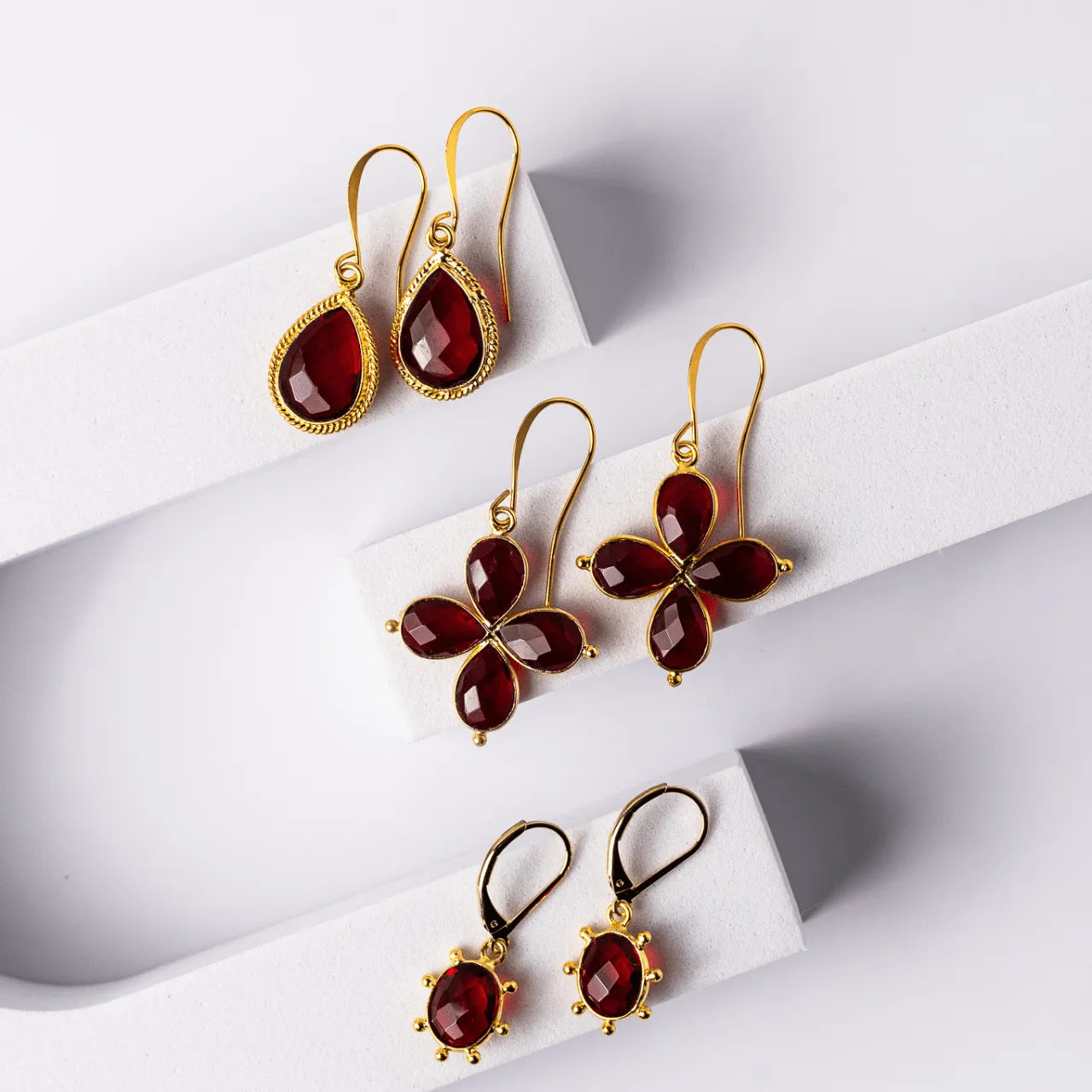 Set of gold earrings with red gemstones on a white surface