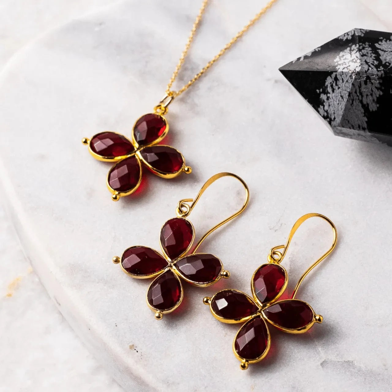Butterfly-shaped earrings with red stones and gold accents on a marble surface.