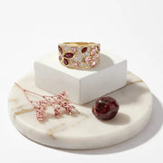 Gold ring with gemstones on a marble stand with decorative elements