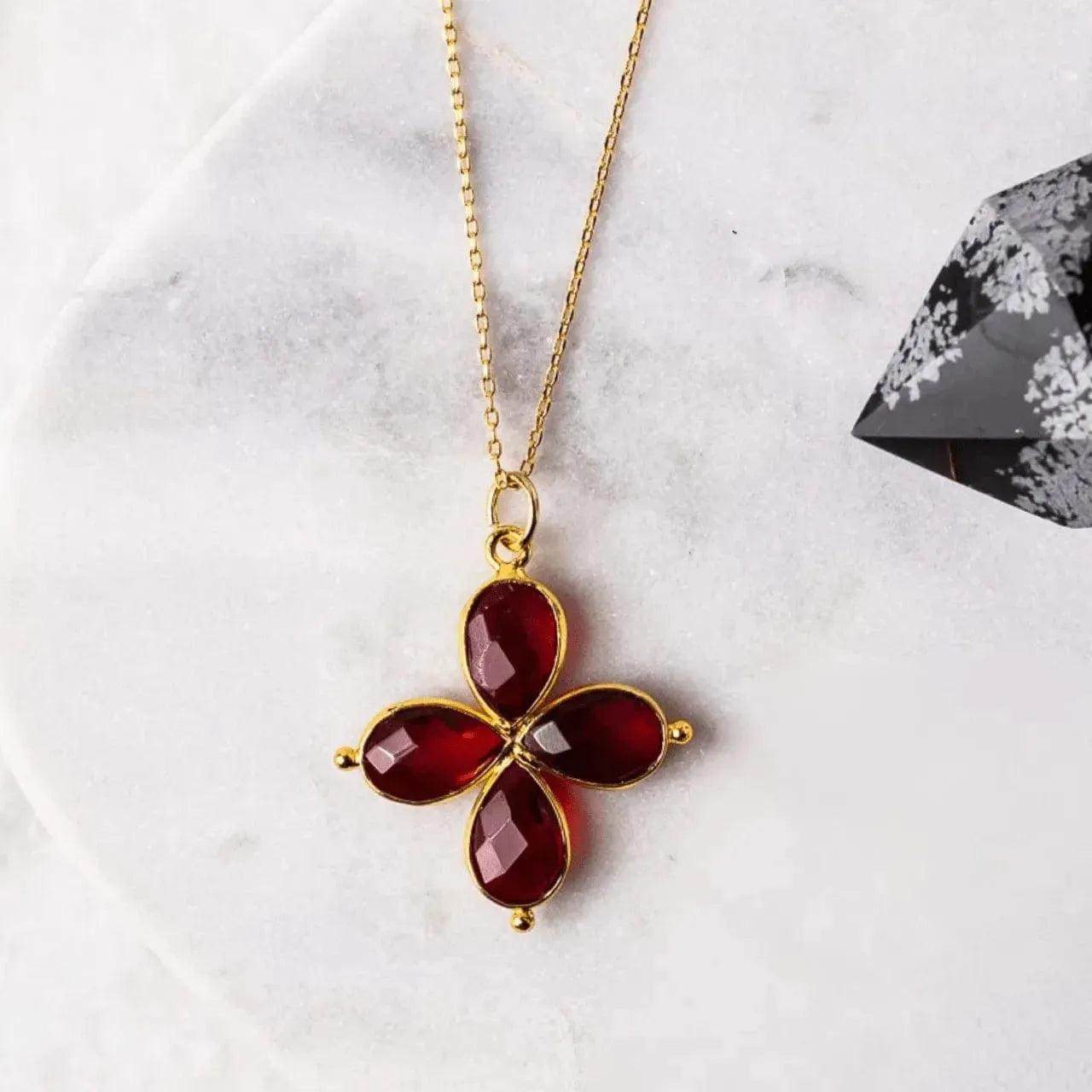 Gold necklace with a red pendant on a marble surface