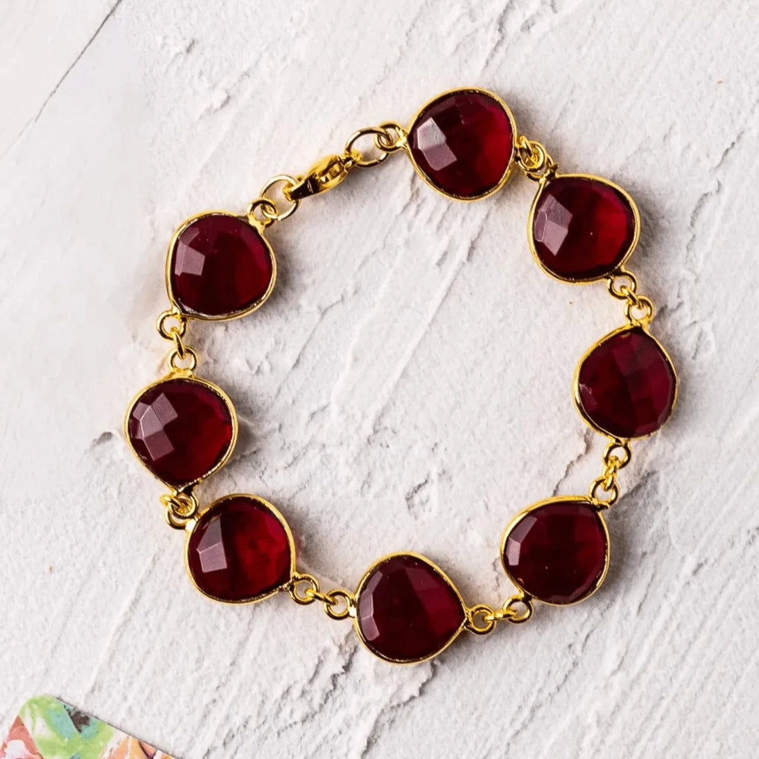 Bracelet with red gemstones and gold chain on a white textured surface