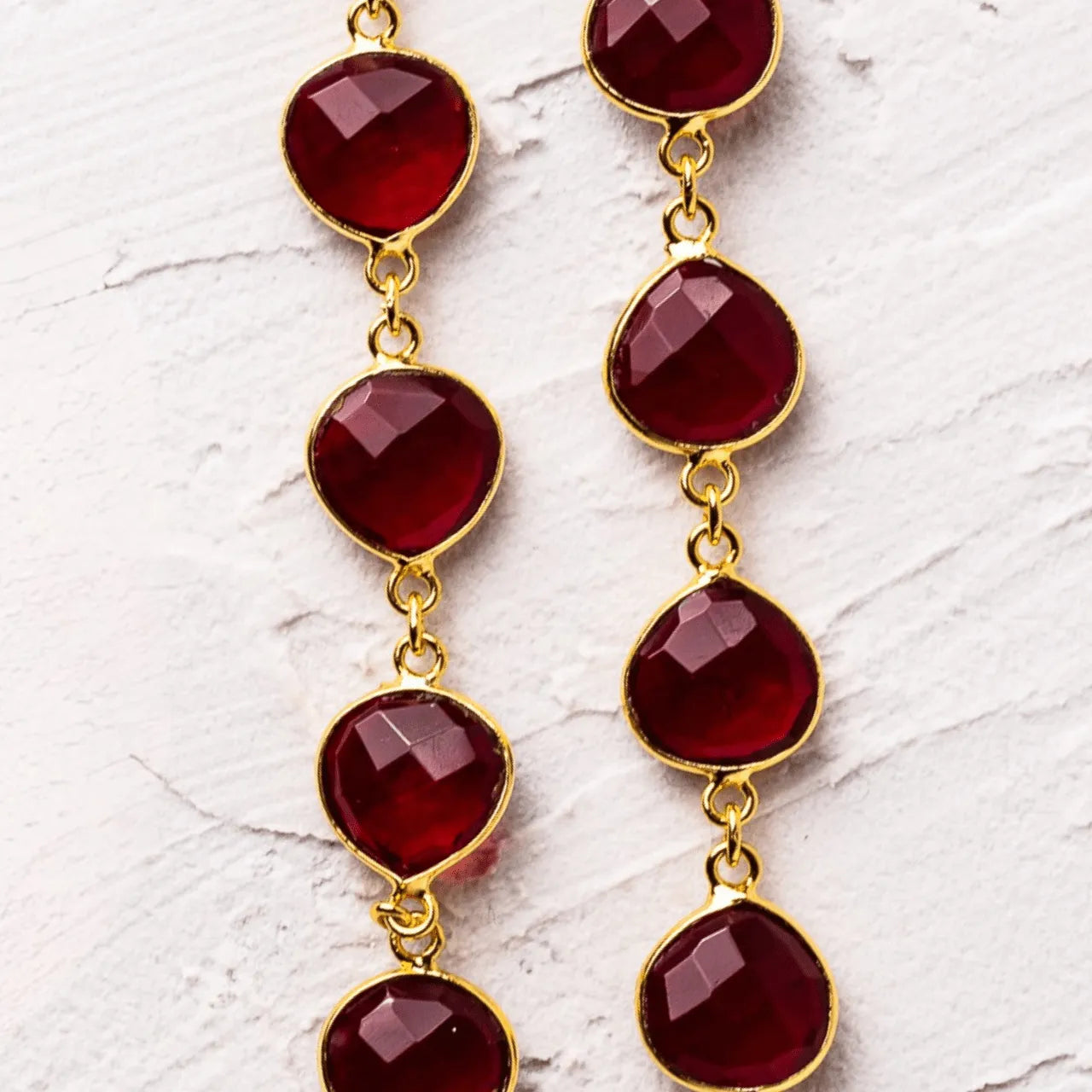 Gold earrings with red gemstones on a white marble surface