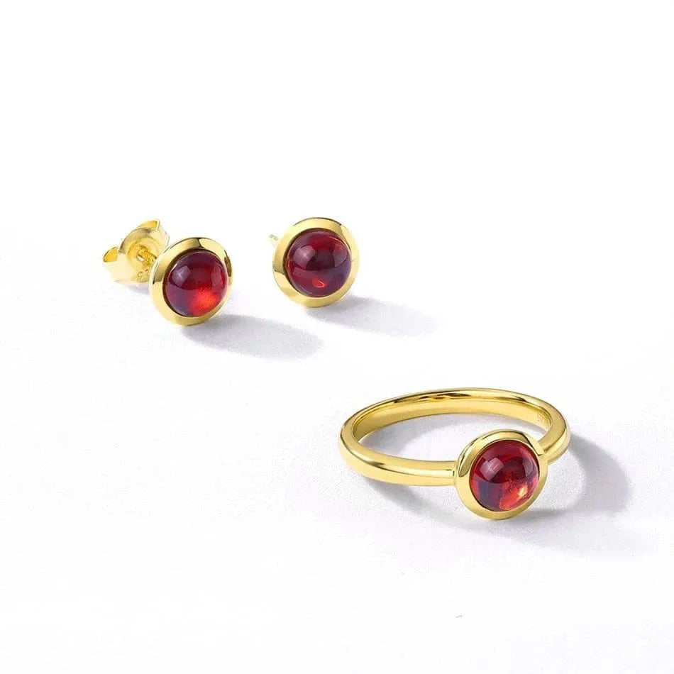 Gold earrings and ring with red gemstones on a white background