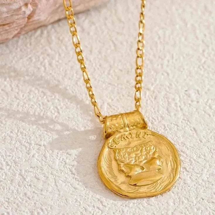 Gold necklace with a coin-shaped pendant on a textured beige surface
