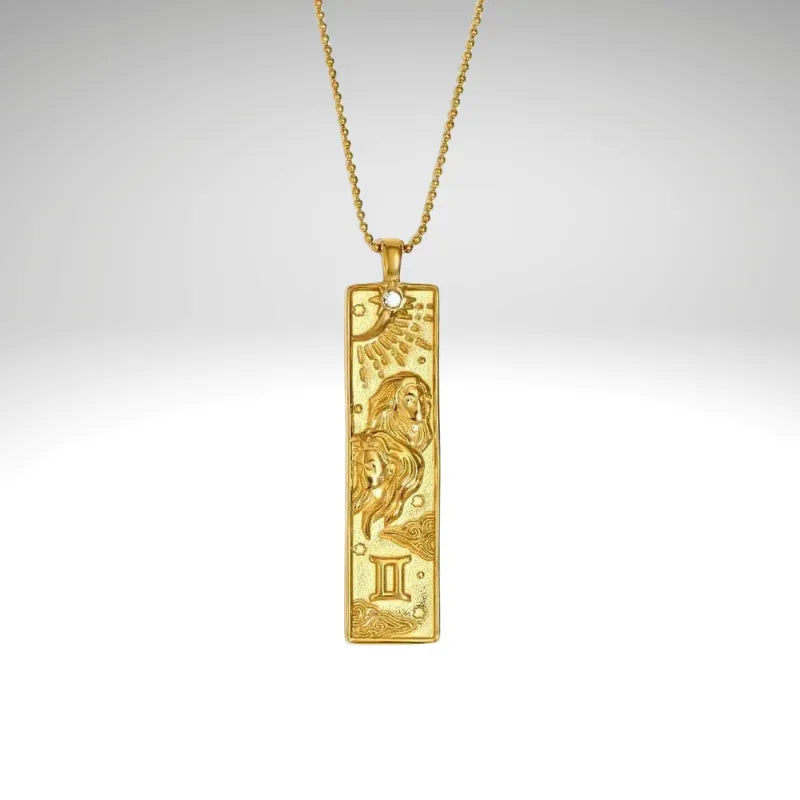 Gold pendant with zodiac design on a chain against a gray background
