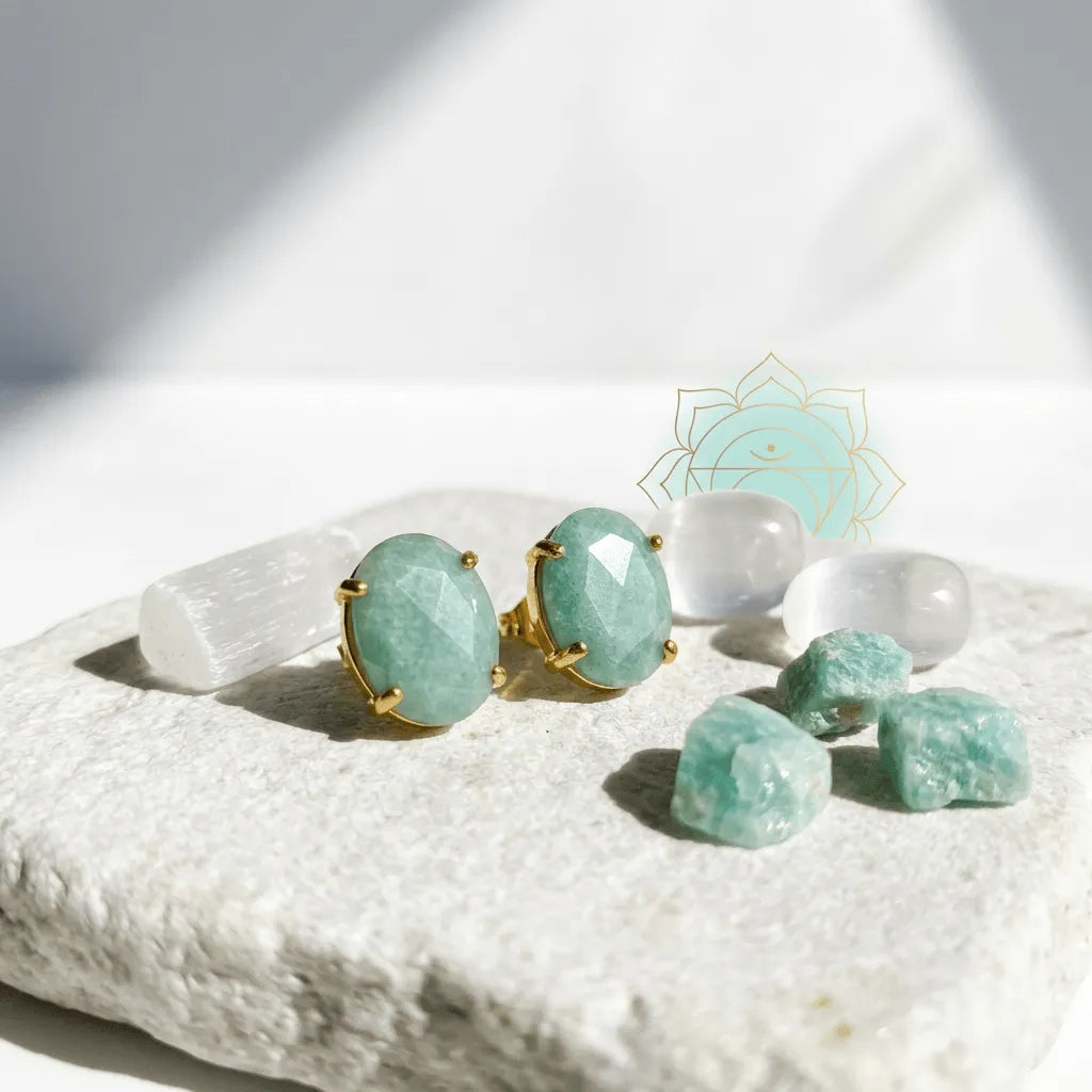 Gold earrings with green gemstones on a white stone surface with additional green stones.