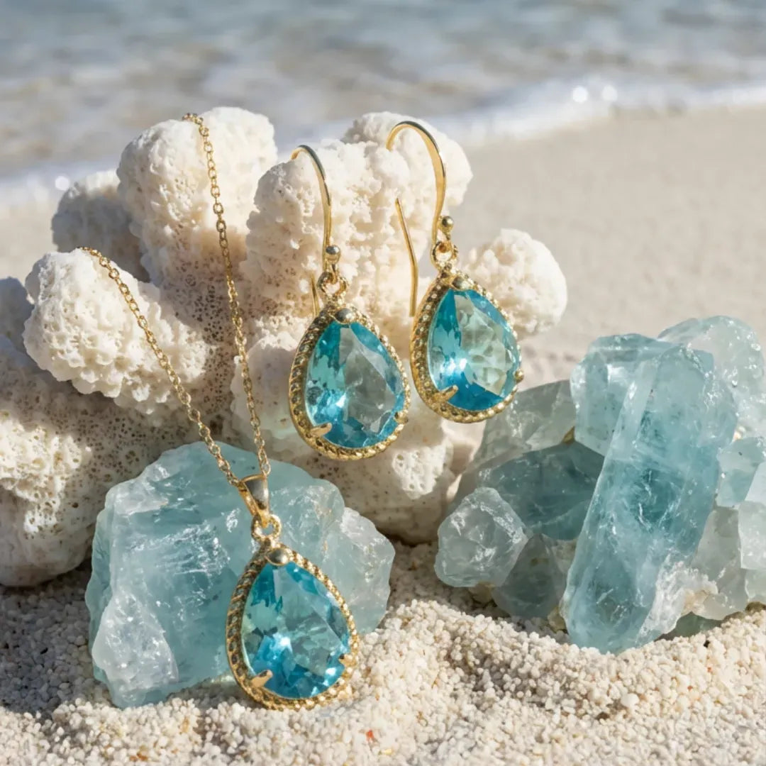 Blue teardrop jewelry set with gold accents on a beach setting with crystals and coral.