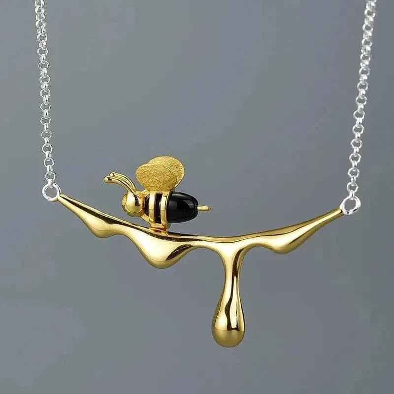 Gold necklace with a bee and olive design on a gray background