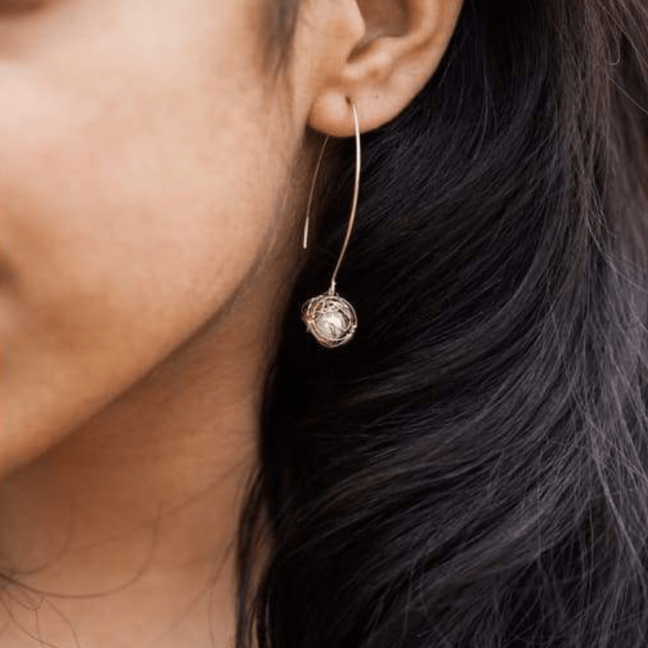 Close-up of a person wearing a gold hoop earring with a decorative element.
