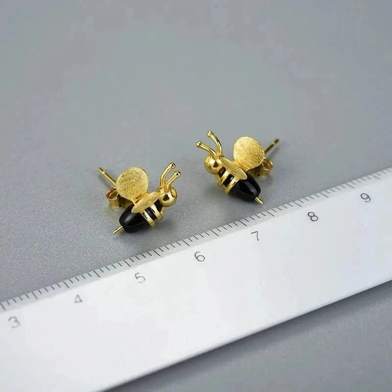 Gold bee-shaped earrings on a gray surface with a ruler for scale.